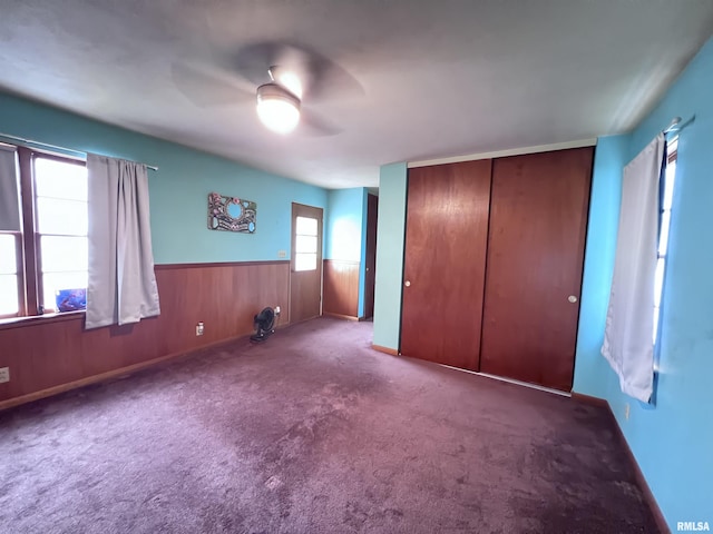 unfurnished bedroom featuring light colored carpet, a closet, wood walls, and ceiling fan