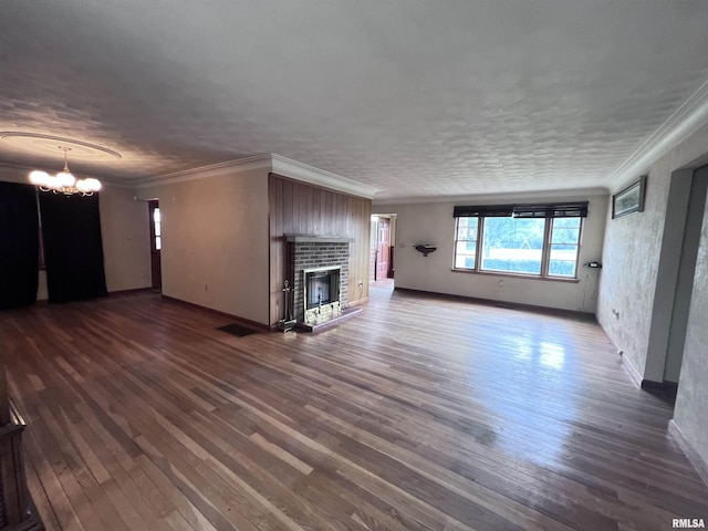 unfurnished living room featuring ornamental molding, hardwood / wood-style flooring, a brick fireplace, and a notable chandelier