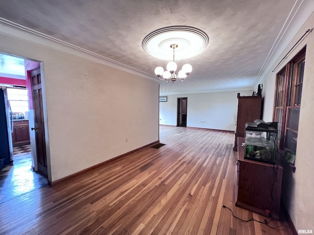 interior space with a chandelier, wood-type flooring, a textured ceiling, and ornamental molding