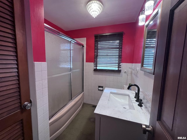 bathroom featuring vanity, bath / shower combo with glass door, and tile walls