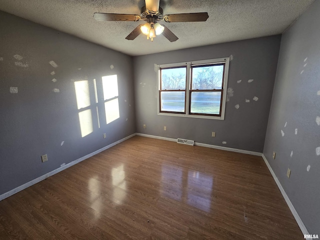 empty room with dark wood-style flooring, visible vents, a textured ceiling, and baseboards