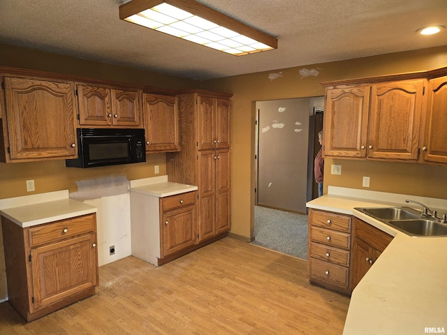 kitchen featuring brown cabinets, black microwave, light countertops, and a sink