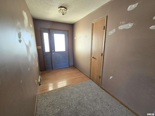 doorway to outside featuring light wood-type flooring, light colored carpet, a textured ceiling, and baseboards