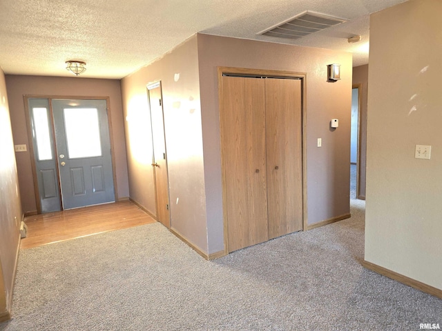 foyer with light carpet, visible vents, a textured ceiling, and baseboards