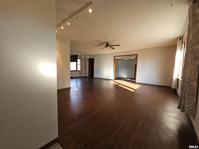 unfurnished room with a textured ceiling, track lighting, dark wood-type flooring, and ceiling fan with notable chandelier