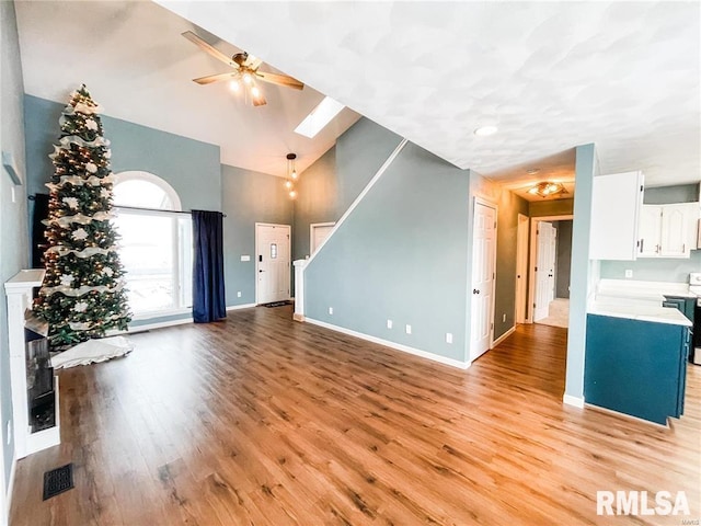 unfurnished living room with a skylight, ceiling fan, light hardwood / wood-style flooring, and high vaulted ceiling