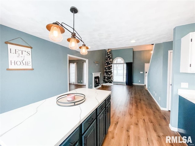 kitchen with white cabinets, light stone counters, light wood-type flooring, and hanging light fixtures