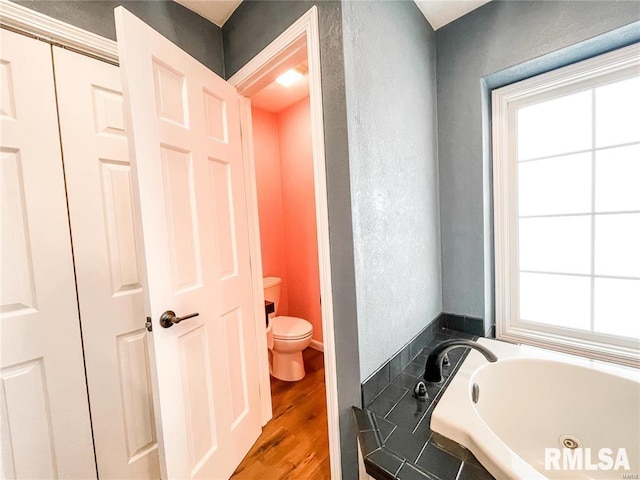 bathroom featuring hardwood / wood-style floors, a healthy amount of sunlight, toilet, and a tub to relax in