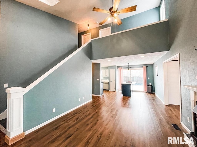 unfurnished living room with ceiling fan, a towering ceiling, and wood-type flooring