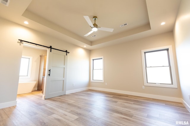 unfurnished room with ceiling fan, a barn door, a raised ceiling, and light hardwood / wood-style floors