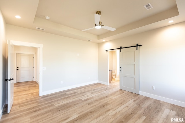 unfurnished room with light hardwood / wood-style flooring, a raised ceiling, ceiling fan, and a barn door