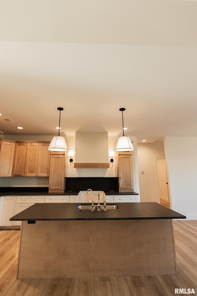 kitchen with pendant lighting, light hardwood / wood-style floors, sink, and a center island with sink