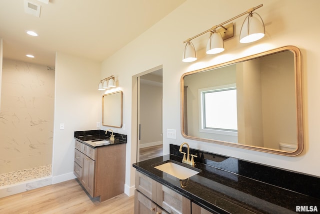 bathroom with wood-type flooring, vanity, and a tile shower