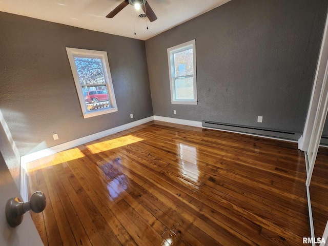 empty room with dark hardwood / wood-style floors, ceiling fan, and a baseboard heating unit