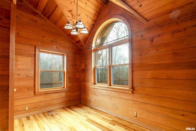 empty room with vaulted ceiling, wooden ceiling, light wood-type flooring, wooden walls, and a notable chandelier