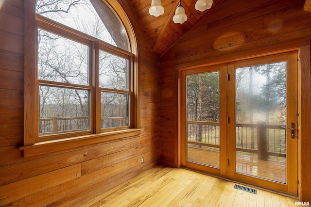 doorway with wooden walls, light hardwood / wood-style floors, vaulted ceiling, and wooden ceiling