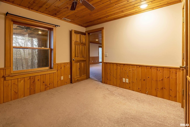 carpeted spare room featuring wooden walls, wooden ceiling, and ceiling fan