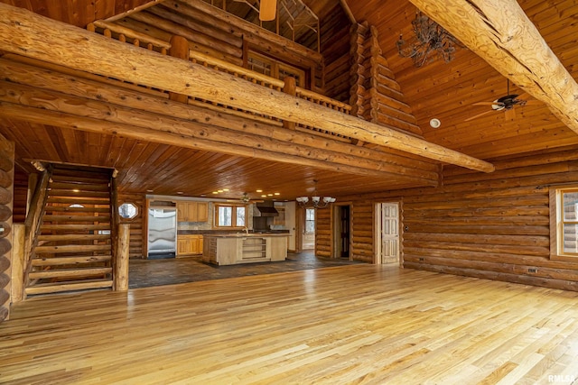 unfurnished living room with rustic walls, a high ceiling, a notable chandelier, wood ceiling, and light wood-type flooring