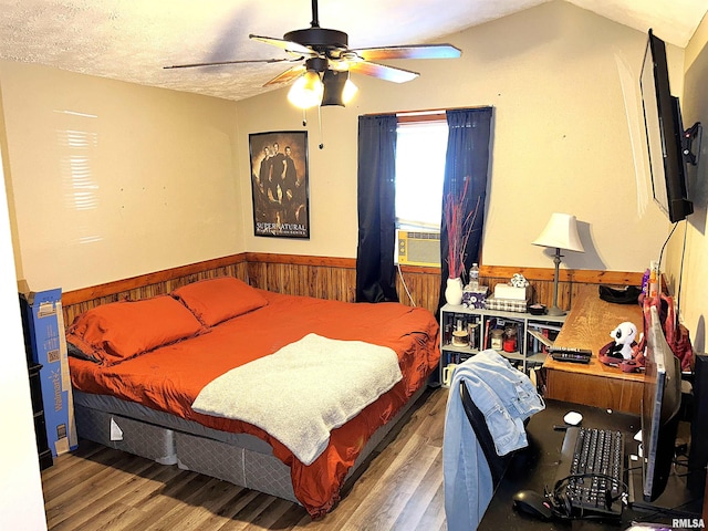 bedroom with ceiling fan, cooling unit, vaulted ceiling, a textured ceiling, and hardwood / wood-style flooring