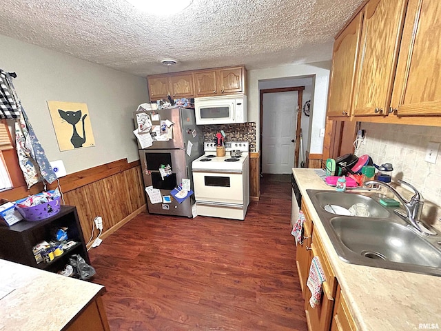 kitchen featuring a textured ceiling, white appliances, dark wood-type flooring, sink, and wood walls