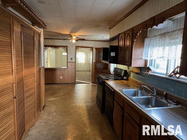 kitchen with backsplash, black appliances, sink, wooden walls, and ceiling fan