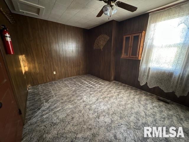 unfurnished room with carpet floors, ceiling fan, and wooden walls