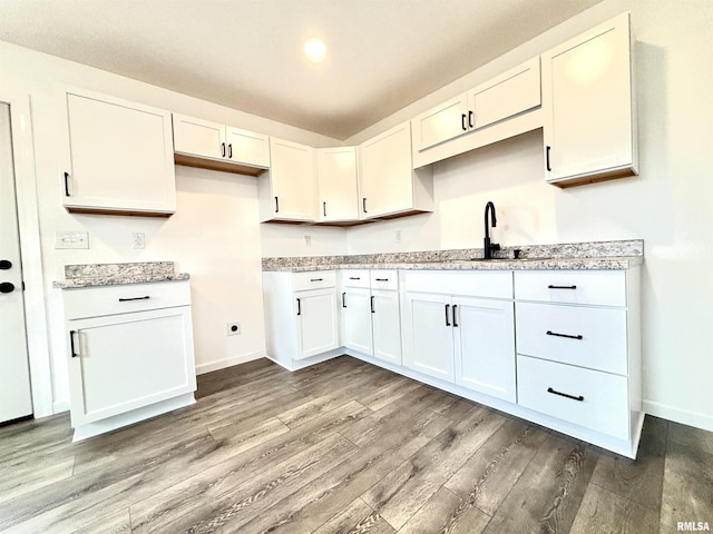 kitchen featuring light hardwood / wood-style floors, light stone countertops, white cabinetry, and sink