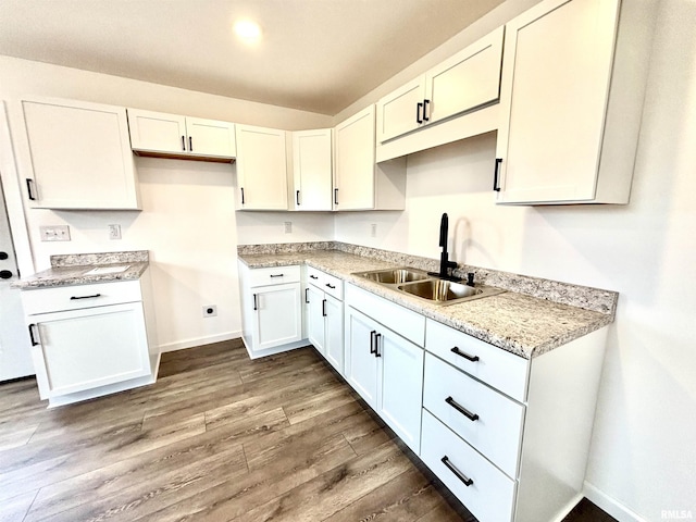 kitchen with light stone countertops, white cabinetry, dark wood-type flooring, and sink