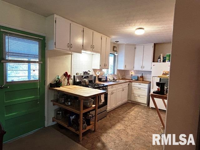 kitchen with tasteful backsplash, white cabinetry, and gas range