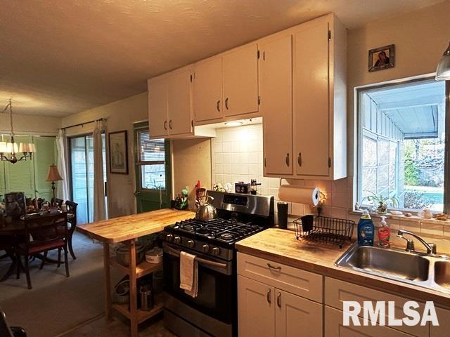 kitchen featuring white cabinetry, stainless steel gas stove, sink, wooden counters, and decorative backsplash