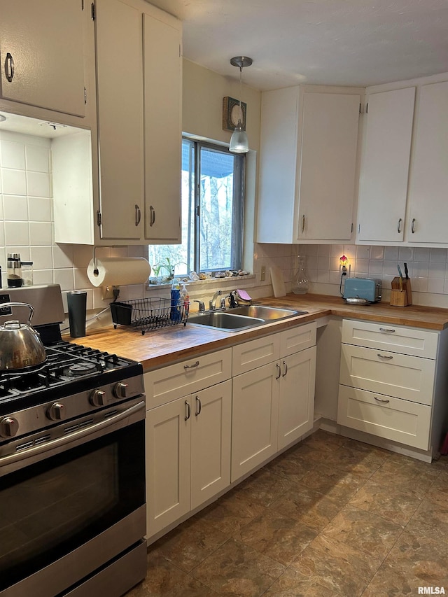 kitchen featuring gas stove, sink, backsplash, pendant lighting, and white cabinets