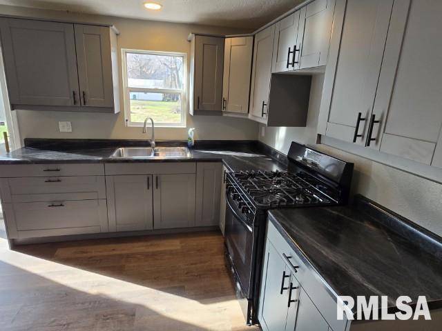 kitchen featuring black range with gas stovetop, dark hardwood / wood-style flooring, gray cabinetry, and sink