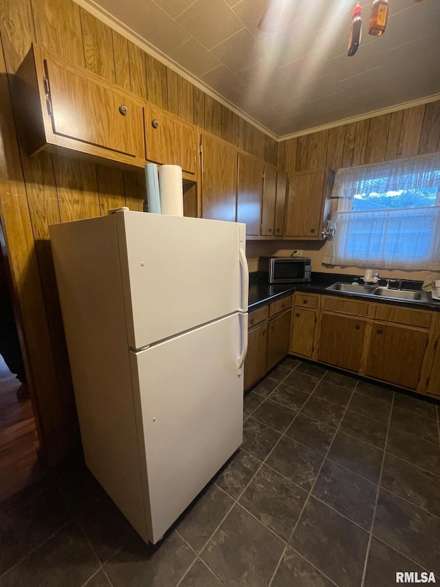 kitchen featuring sink, wood walls, white fridge, dark tile patterned flooring, and ornamental molding