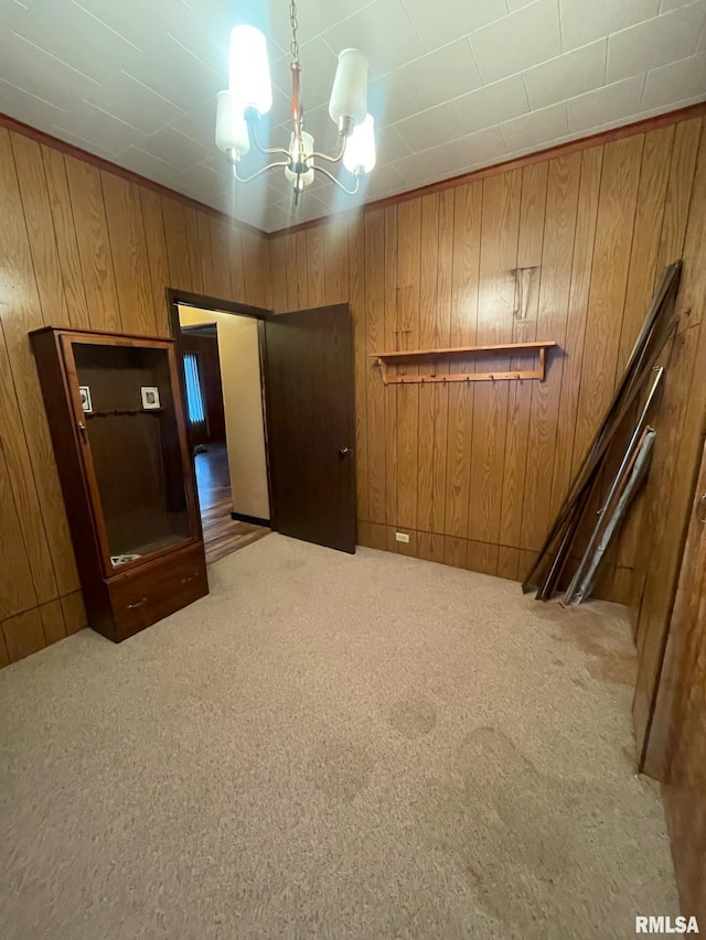 unfurnished bedroom with wood walls, carpet, and an inviting chandelier