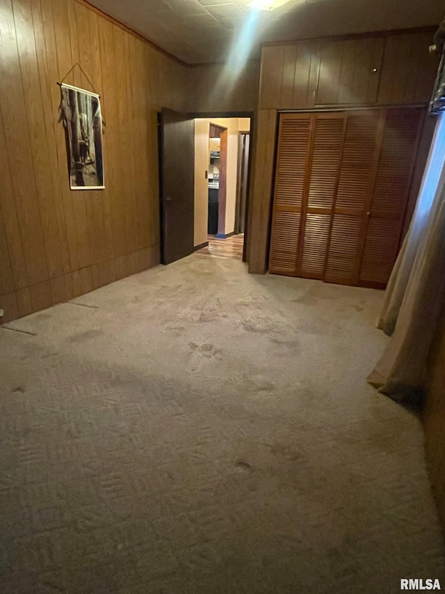 unfurnished bedroom featuring light carpet, a closet, and wood walls