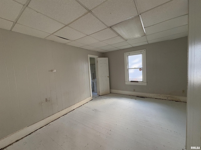 spare room with a drop ceiling, wooden walls, and light hardwood / wood-style flooring