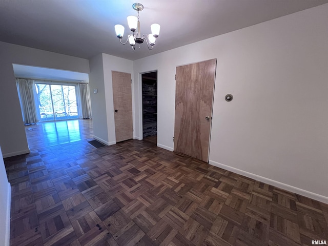 empty room featuring a notable chandelier and dark parquet flooring