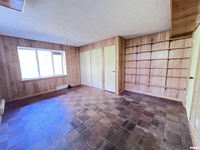 unfurnished bedroom with a textured ceiling, a baseboard radiator, and wood walls