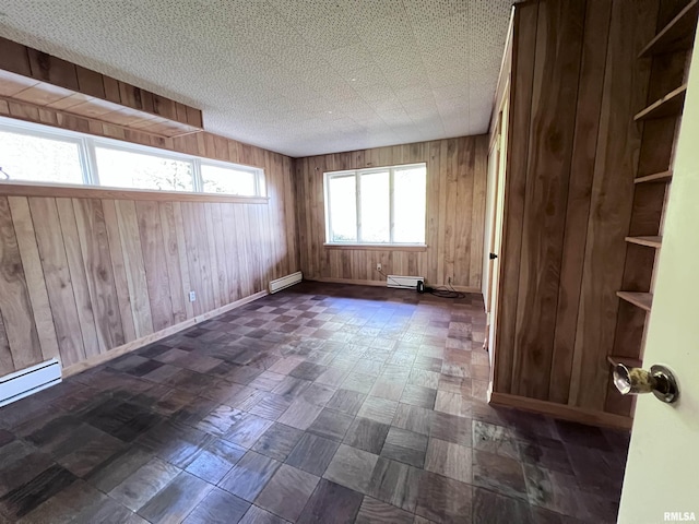 spare room featuring wooden walls, a baseboard radiator, and a textured ceiling