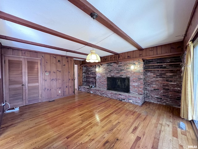 unfurnished living room with beamed ceiling, light wood-type flooring, wooden walls, and a brick fireplace