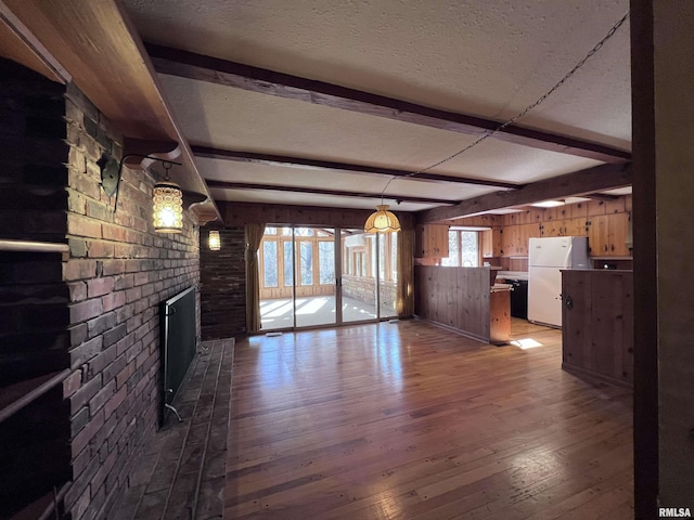 unfurnished living room featuring a brick fireplace, a textured ceiling, wooden walls, beamed ceiling, and light hardwood / wood-style floors