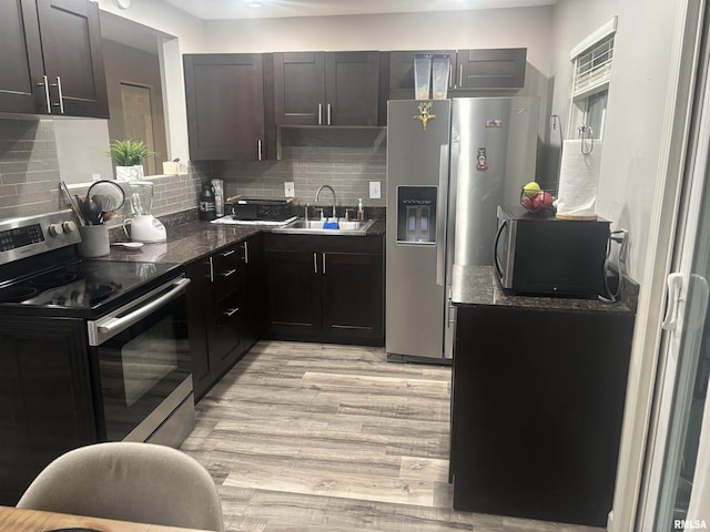 kitchen with sink, dark stone counters, light hardwood / wood-style floors, decorative backsplash, and appliances with stainless steel finishes