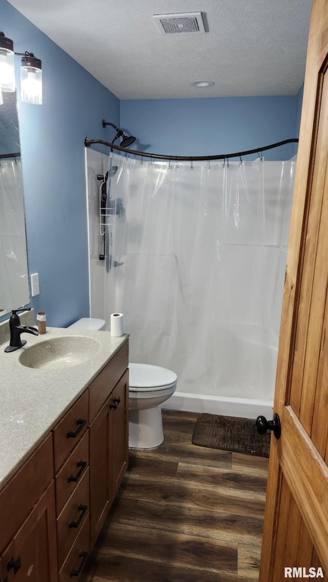 bathroom with walk in shower, vanity, a textured ceiling, hardwood / wood-style flooring, and toilet