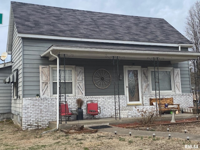 view of front of property featuring a porch, a shingled roof, and brick siding