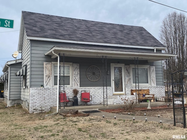 view of front facade featuring covered porch, roof with shingles, and brick siding