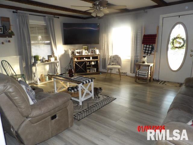 living area featuring beamed ceiling, wood finished floors, and a ceiling fan