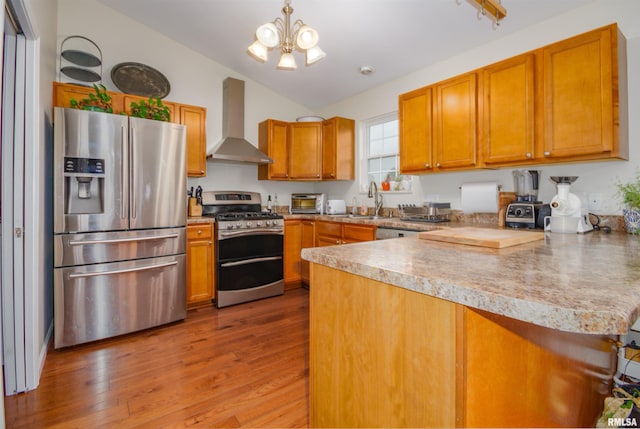 kitchen with vaulted ceiling, wall chimney exhaust hood, light wood-type flooring, appliances with stainless steel finishes, and kitchen peninsula