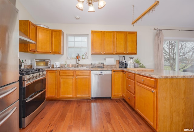 kitchen with ventilation hood, sink, light hardwood / wood-style flooring, kitchen peninsula, and stainless steel appliances