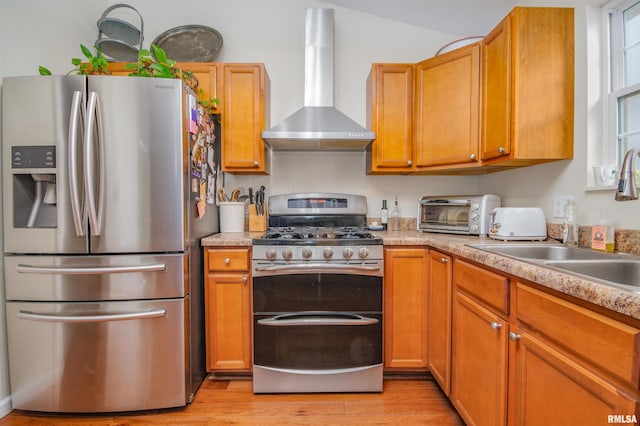 kitchen with stainless steel appliances, vaulted ceiling, sink, wall chimney range hood, and light hardwood / wood-style flooring