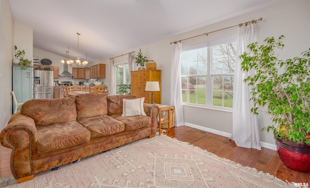 living room with a chandelier, light wood-type flooring, plenty of natural light, and lofted ceiling